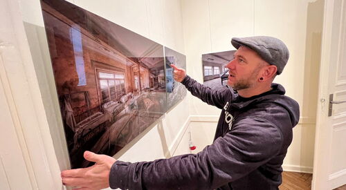 In einem Ausstellungsraum. Mann steht vor Bild / Fotographie eines alten verwahrlosten Bettenhauses.