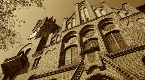 Außenansicht eines Gebäudes aus einem niedrigen Blickwinkel, aufgenommen in Sepia-Tönen. Der Fokus liegt auf der Architektur, insbesondere auf den hohen Türmen und den dekorativen Fenstern.