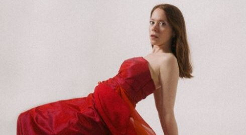 Frau in roten schulterfreien Kleid mit langen Haaren. In Pose.