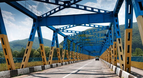 Blaue Stahlbrücke mit Fahrbahn und Geländern, Blick entlang der Brücke in die Ferne.