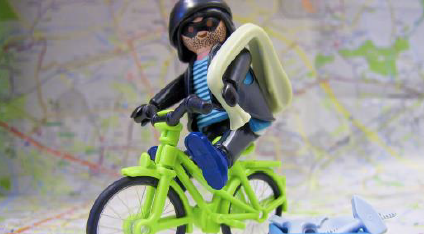 Kleines grünes Spielzeugfahrrad auf dem ein Räuber sitzt ein kleiner Spielzeug Werkzeugkoffer steht daneben.