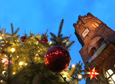GroÃŸer Weihnachtsbaum geschmÃ¼ckt mit roten Kugeln und Lichtern, von unten fotografiert. Die Turmuhr des alten Rathaus in Babendberg.