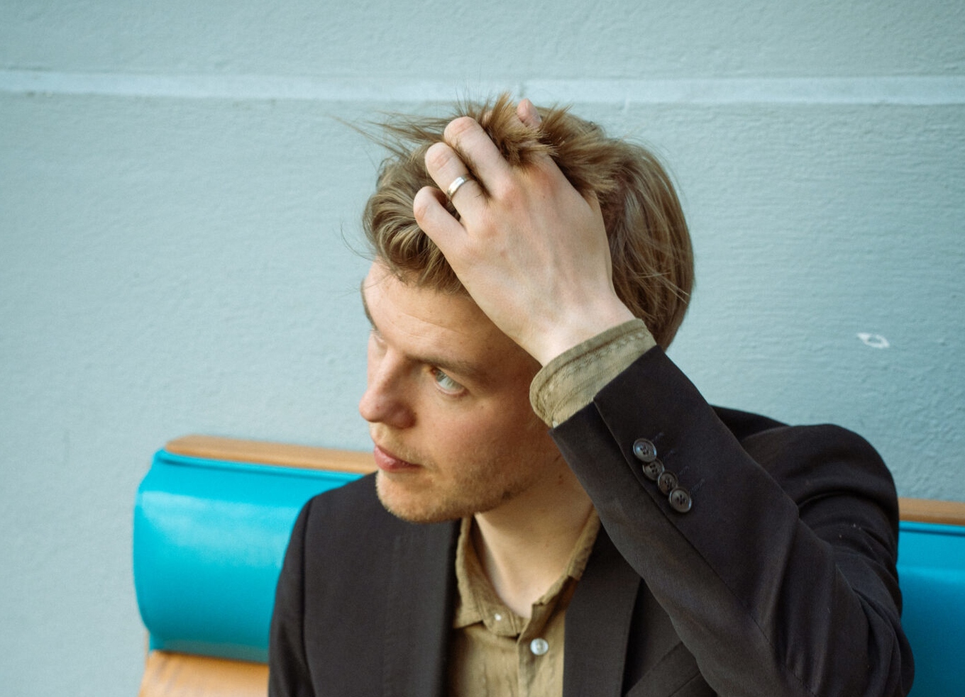 Portrait: Mann mit dunkel-blonden Haaren der sich mit der linken Hand ins Haar greift.